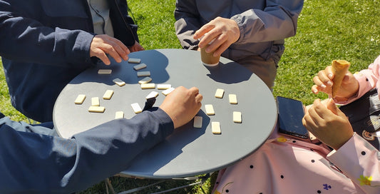 People are playing dominoes around a table outside.
