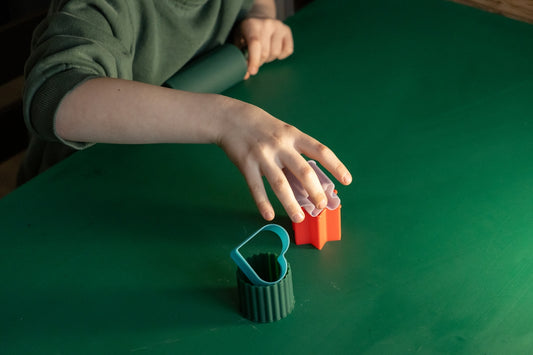 Child's hands playing with cookie cutters on green table